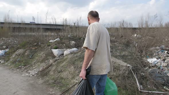 Man Walking along Garbage Dump with Trash Bins alt