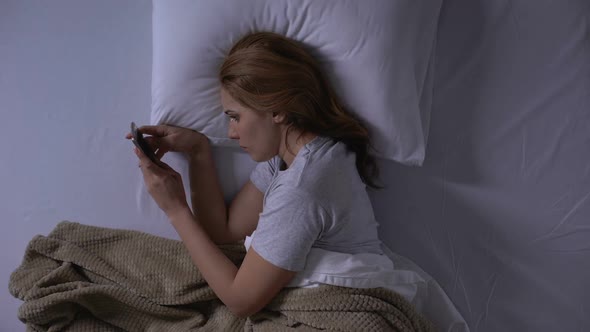 Sad Woman Crying Reading Old Messages on Smartphone Lying in Bed, Memories alt