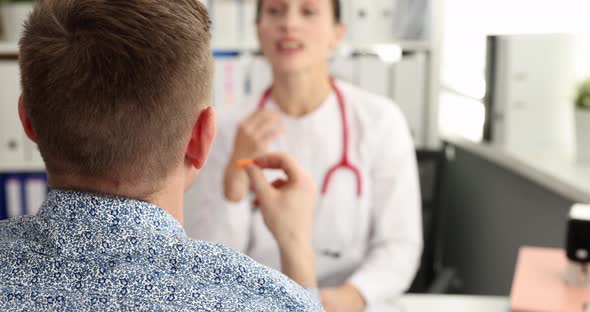 Male Patient Inserting Earplugs Into His Ears While Talking with Doctor in Clinic  Movie alt