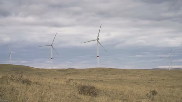 Motion the Blades of a Large Wind Turbine in a Field Against a Background of Cloudy Grey Sky on the