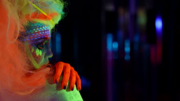 Eccentric Woman with Fluorescent Paint on Face and Body in Nightclub Side Portrait in Darkness alt