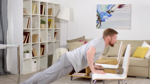 Athletic Man Doing Push Ups on Two Chairs while Training at Home alt