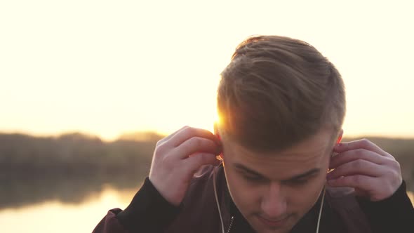 Young Handsome Manwearing Headphones Listens to Music on Beach During Sunset