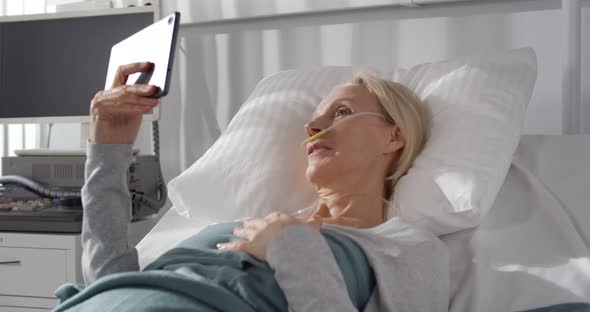 Aged Female Patient with Breathing Tube Having Video Call on Tablet Pc Lying in Hospital Bed alt