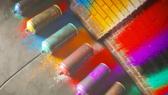 Used, colorful spray paint cans rolling in front of a painted brick wall. 4KHD alt