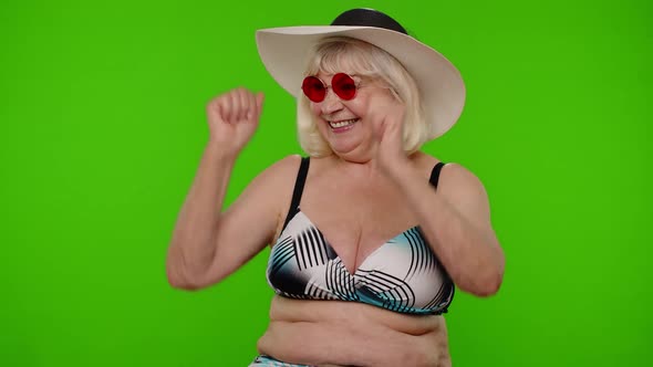 Senior Woman Tourist in Sunglasses Looking at Camera Dancing Celebrating on Chroma Key Background alt