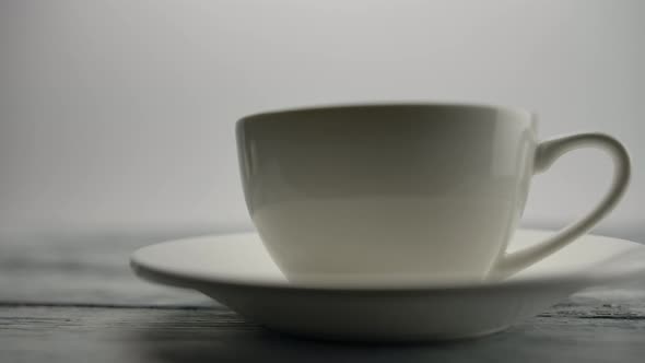 Human Hand Puts a Transparent Teapot on the Wooden Table Behind Classic Cup alt