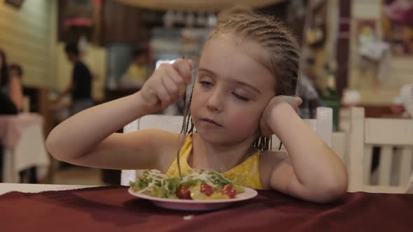 Little Girl Eat Green Salad with Appetite in the Restaurant. Good Health Concept