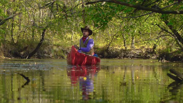 Cowboy in a Canoe Floats on the River in the Forest alt