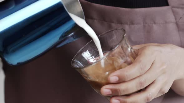 Close up shot of professional barista pouring milk from pitcher making beautiful Latte art coffee