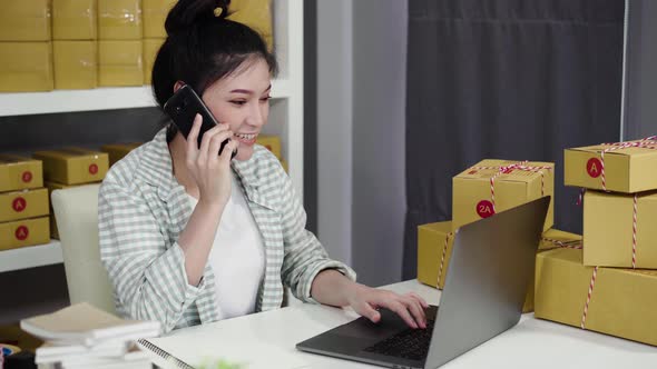 young woman talking on smartphone and use computer laptop to selling product online from home office