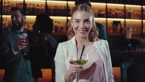 Smiling blond woman toasting in a cocktail bar