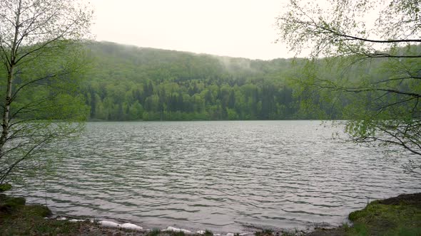 Enigmatic lonely man sitting on bench on lake shore in the mountain forest. Lake Sf. Ana Romania alt