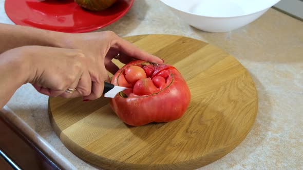 Woman's hands using kitchen knife cutting clumsy, ugly, juicy tomato on wooden cutting board