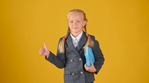 teenage schoolgirl in a school uniform with books in her hands showing thumbs up