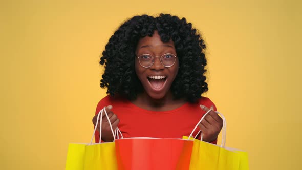 Positive Black Woman Opening Shopping Bags and Saying Wow alt