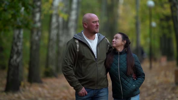 Portrait of Middle-aged Spouses at Walking in Autumn Park, Loving Man and Woman Are Embracing and alt