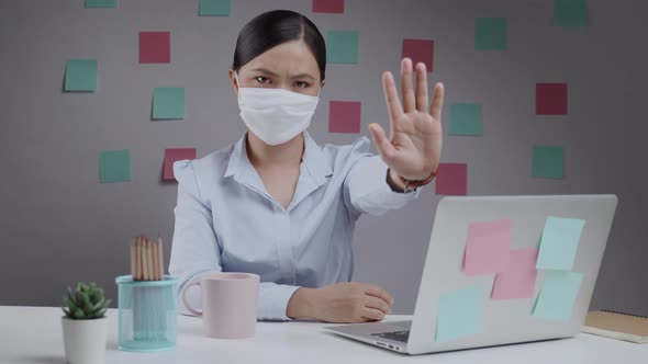 Asian woman wearing protective face mask showing hand making stop sign