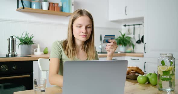 Woman Pays Online By Credit Card Using Laptop in Kitchen. Customer Buys at Home