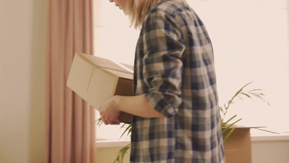 A Young Woman Brings a Cardboard Box with Clothes and Things Into the Room