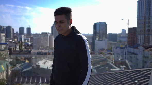 Live Camera Follows Confident Middle Eastern Young Man Walking on Rooftop in Urban City Posing alt