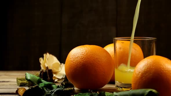 Orange Juice And Three Oranges Are Poured Into A Glass Next To Them On A Table With Flowers