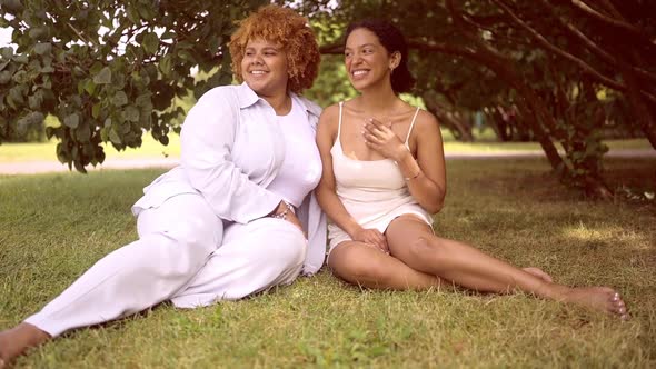 Lovely Beautiful Happy Lesbian African American Couple Sitting on Green Grass Hugging Outside at