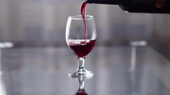 Red Wine Is Poured From a Bottle Into a Glass Against the Background of a Window alt