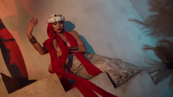 a Blonde in a Turban and a Shiny Dress Sits on the Stairs and Moves Hands Beautifully with a Red alt