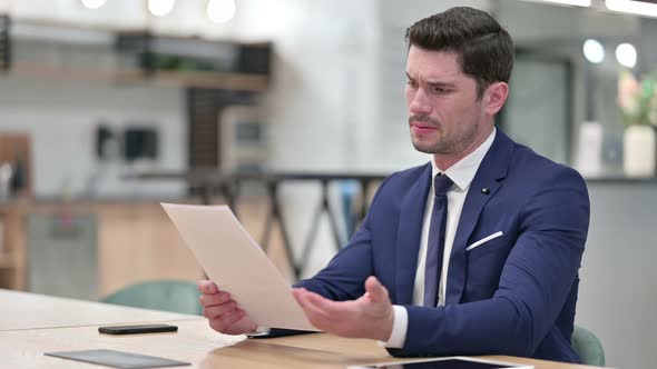 Disappointed Businessman Reading Documents in Office  alt