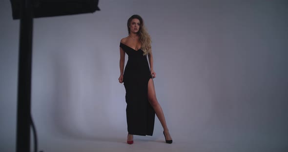 The Girl Poses Lying on the Ground in a Black Dress Wrapping Her Arms Around Her Waist alt