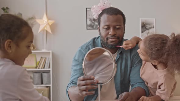 Two Little Girls Applying Make Up on Dads Face alt