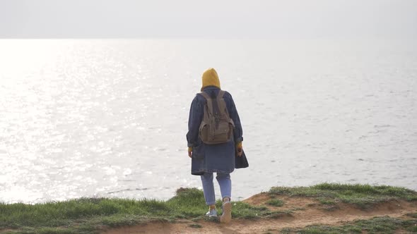 A Woman Traveler with a Large Backpack in Warm Clothes Approaches the Endless Sea