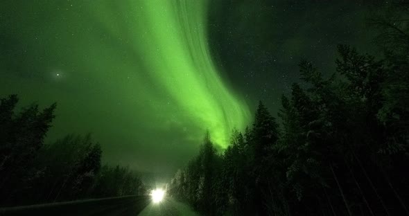 Timelapse of the Northern Lights Against the Background of a Forest and a Road with Passing Cars