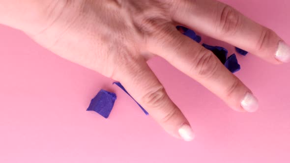 4k video, a woman's hand removes torn crumpled purple pieces of paper on a pink background from the