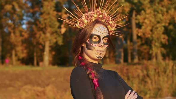 A Young Woman with Santa Muerte Makeup Dressed in a Black Dress of Death Walks Against the Backdrop alt