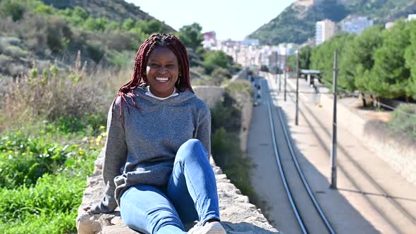 Young Black Sits Near the Railways and Smiles Broadly