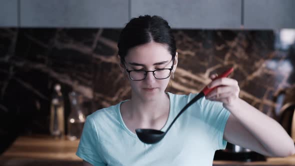 Happy Teen Tasting Soup on Spoon in Modern Kitchen and Smiling alt