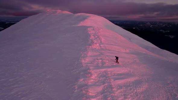 Drone Circle Around Man Moving on Mountain Ridge Covered in Snow During Sunrise