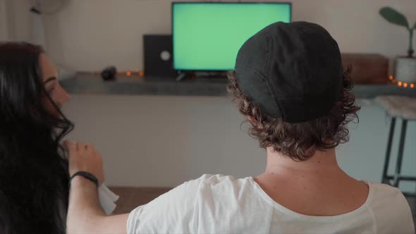 Man and Woman Sitting on Couch Looking at Green Screen alt