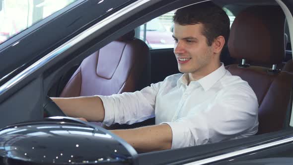 A Young Man Holds the Steering Wheel of a New Car alt