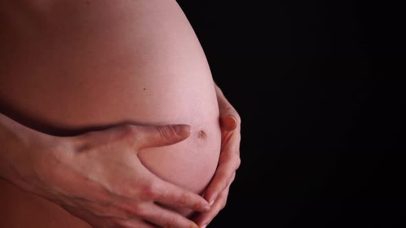 Pregnant woman caressing her belly, closeup on black