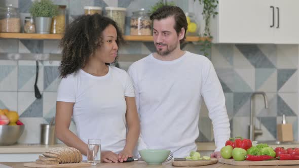 Serious Mixed Race Couple Talking While Standing in Kitchen alt