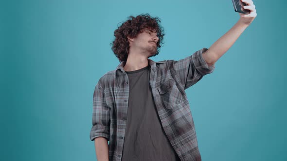 The Young Man with Curly Hair Participates in a Video Call Smiles Broadly on the Phone and Shows the alt