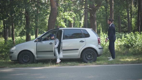Wide Shot Woman Walking Out Driver's Seat Helping Man Pushing Vehicle on Suburban Roadside on Sunny alt