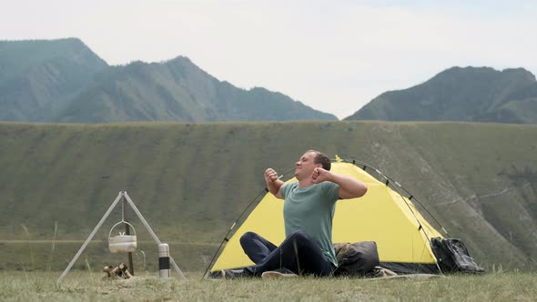 Male Tourist Pulls His Hands Up Waking Up in the Morning in Front of the Tent While Resting. alt