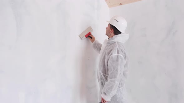 A Man in a Protective Suit Applies Putty on the Walls to Align the Walls