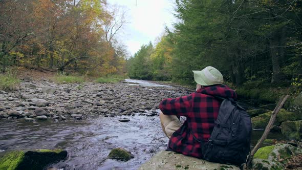 An older hiker resting by a creek in a scenic forest in the mountains. alt