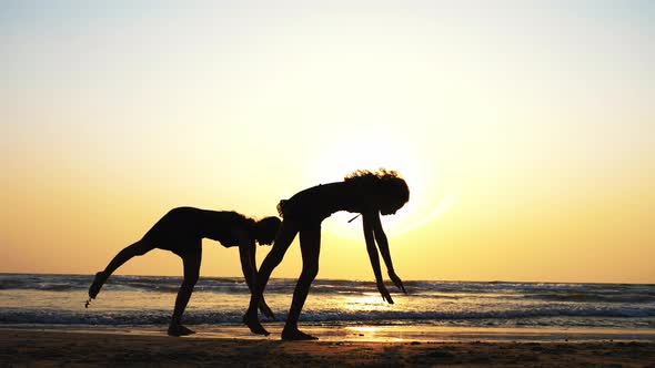 Silhouette of Sporty Young Women Practicing Acrobatic Element on the Beach