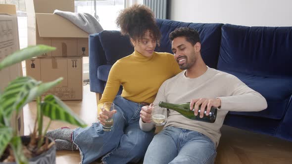 Couple In New Home Celebrate With Champagne Sitting On Floor In Lounge On Moving Day Boxes